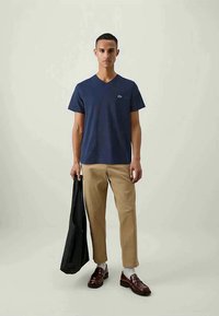 Tricou din bumbac de culoare bleumarin, cu guler în V, având un mic logo pe piept, asortat cu pantaloni bej și pantofi maro.