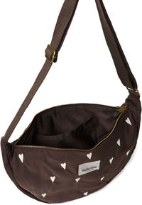Bruine stoffen crossbody tas met witte hartpatronen, gouden rits en verstelbare schouderband. Binnenin heeft de tas een pocket en een zachte voering.
