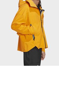 Gelbe wasserdichte Jacke mit Kapuze, ausgestattet mit einem Frontreißverschluss, Seitentaschen, elastischen Bündchen und schwarzen Akzenten. Leichtes, langlebiges Design.