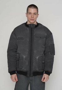 Zwarte pufferjas met ritssluiting, twee steekzakken aan de voorkant en geribde manchetten. Voorzien van een gestructureerd oppervlak en geborduurd merkembleem.