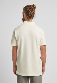 Crème-kleurige polo, korte mouwen, zachte textuur, klassieke kraag en een rechte snit. Geen zichtbare patronen of hardwaredetails.