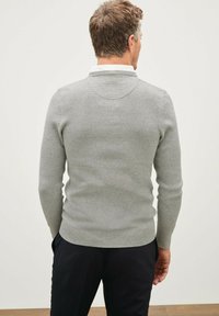 Pull en maille grise avec une texture côtelée, des manches longues et un col subtil. Le dos présente un design ajusté aux lignes épurées.