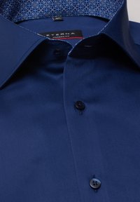 Marineblauw overhemd met een moderne pasvorm, voorzien van een gestructureerde kraag, donkere knopen en een patroon in lichtblauw aan de binnenkant van de kraag.