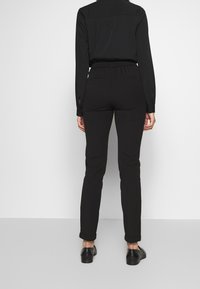 Mustat istuvat housut joustavalla vyötärönauhalla, käännetyin lahkeensuilla ja sileällä, mattapintaisella tekstuurilla. Takakuvassa näkyy siisti ja yksinkertainen muotoilu.