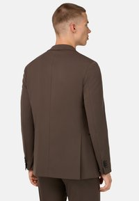 Ruskea sovitettu pukujakku, jossa on sileä pinta, yksittäinen venttiili ja neljän napin hihasetelit. Takana näkyvä leikkausmuoto.