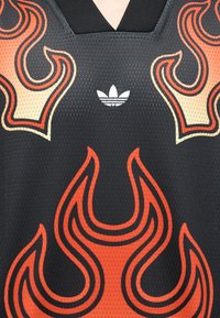 Μαύρη αθλητική μπλούζα από δίχτυ με μεγάλα κόκκινα και πορτοκαλί σχέδια φλόγας και λευκό λογότυπο Adidas trefoil τοποθετημένο στο κέντρο κοντά στο λαιμό.