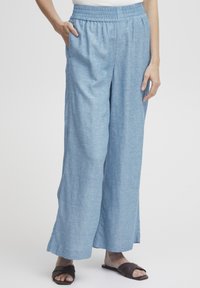 Svijetloplave široke hlače od teksturirane tkanine, s elastičnom waistbandom i bočnim džepovima, uparene s smeškim sandalama.