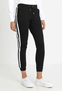 Svarta sweatpants med vita sidostråkar, tillverkade av mjukt tyg, med en elastisk midja med dragsko och ribbade muddar.