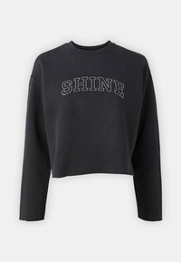 Svart cropped sweatshirt laget av myk stoff. Har lange ermer og ordet "SHINE" i sølvbroderi over brystet.
