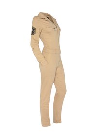 Mono beige con cremallera frontal, cuello y cinturón. Incluye dos bolsillos en el pecho y un parche en la manga izquierda con rayas. Corte ajustado.