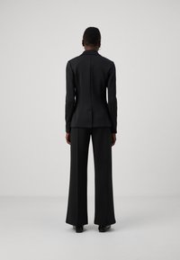 Svart skräddarsydd kostym med en strukturerad kavaj och vida byxor, tillverkad av ett mjukt tyg. Slimmad passform med en enskild slitsdetalj bak.