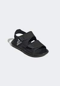 Sort atletisk sandal med en tekstureret sål, justerbare stropper og et ventileret design med Adidas-branding på siden.