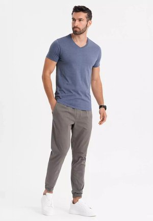Camiseta de cuello en V azul en una tela suave, combinada con pantalones jogger gris claro con puños elásticos y zapatillas blancas, creando un atuendo casual.