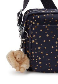 Bolsa de tela de color azul oscuro con un patrón de estrellas doradas, que presenta un llavero de mono suave y peludo, y un bolsillo lateral. Materiales duraderos con un diseño práctico.