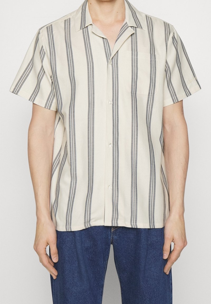 Camisa de manga corta en tela beige claro con rayas verticales grises, cuello con muesca, bolsillo frontal y cierre con botones.