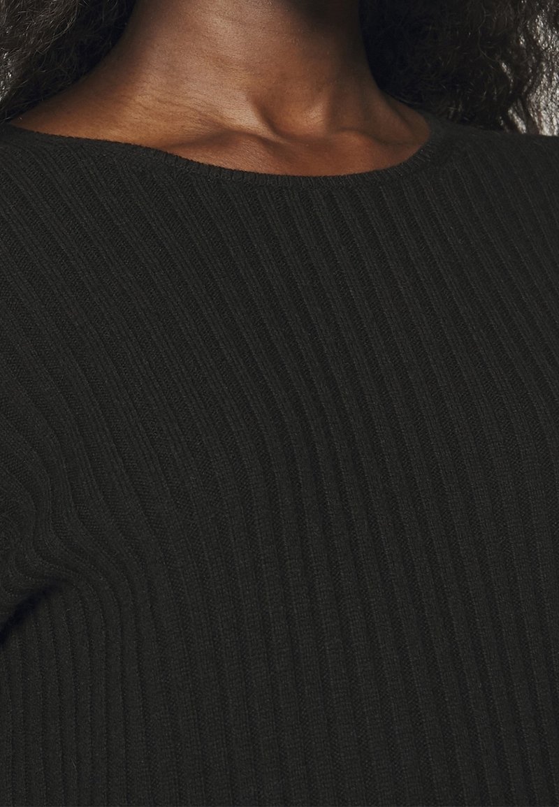 Gros plan sur un tissu noir côtelé, présentant une texture lisse avec un col arrondi. Le motif est uniforme et subtil sur toute la surface.