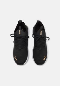 Svarte joggesko med et teksturert mesh-overdel, med gull detaljer og snøringer, og en hvit mellomsole. Puma-logo på siden og tungen.