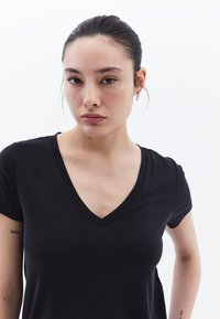 T-shirt nera a maniche corte con scollo a V, realizzata in tessuto morbido, forma aderente, con un design classico e senza motivi o dettagli visibili.