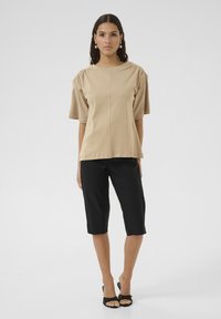Beige top met korte mouwen en geplooide schouders, gecombineerd met zwarte cropped broek, gedragen met zwarte open teen hakken. Eenvoudig ontwerp, gladde textuur.