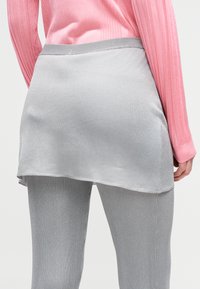 Γκρι φούστα με επίπεδα και ομαλή υφή, με μακρύτερο πίσω τελείωμα. Συνδυασμένη με γκρι ριμπ κολάν και ροζ μακρυμάνικη μπλούζα.