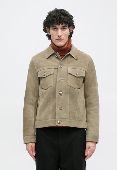 Χακί σουέτ μπουφάν με γιακά, δύο τσέπες στο στήθος, τέσσερις μπροστινούς κουμπιά και ίσια γραμμή. Φορεμένο πάνω από σκούρο ριμπ ζιβάγκο.