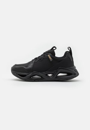 Baskets de sport noires avec empeigne en mesh et cuir, semelle épaisse sculptée avec détails découpés, fermeture à lacets à l'avant et languettes au talon et à la languette.