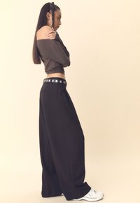 Czarne spodnie o szerokich nogawkach z wysokim stanem i srebrnymi ćwiekami na pasku. Połączone z ciemnobrązową bluzką z odkrytymi ramionami i białymi tenisówkami.