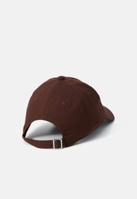 Brown cotton baseball cap with a curved brim, adjustable strap, and ventilation eyelets. Visible stitching on the top and rear.