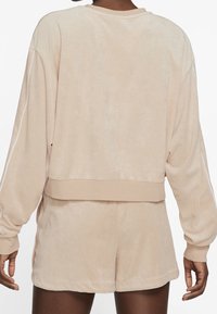 Beige lounge-set i mjukt tyg; innehåller en cropped, oversized tröja och matchande shorts med en slät yta och enkel design.