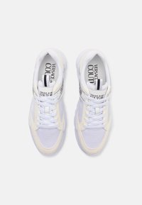 Scarpe sportive bianche che presentano un mix di materiali in rete e suede, con chiusura a lacci e accenti di branding neri sulla linguetta e sui lati.
