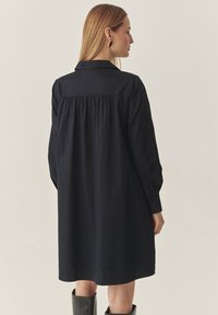 Pikendustega, tumesinise värvi kleit, mis on valmistatud kergest kangast. Omab krae kaelust ja gathered seljaosa detaili, mis loob mugava silueti.