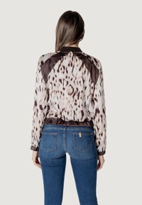 Giacca bomber colorata con motivo leopardato, dettagli marroni, vita elasticizzata e maniche lunghe. Abbinata a jeans in denim blu.