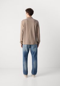 Langermet beige skjorte med krage, kombinert med lyseblå denimjeans. Skjorten har et strukturert mønster; jeansene er litt falmede.