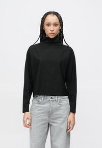 Černý krátký rolák s dlouhými rukávy, vyrobený z hladké látky. Kombinován se světle šedými volnými džínami. Jednoduchý design bez vzorů.