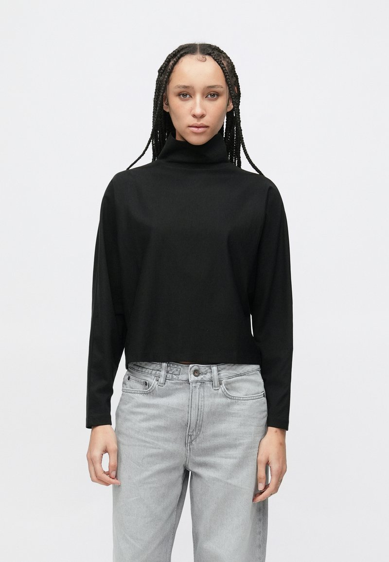 Černý krátký rolák s dlouhými rukávy, vyrobený z hladké látky. Kombinován se světle šedými volnými džínami. Jednoduchý design bez vzorů.