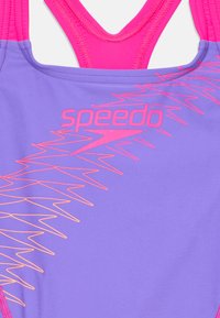 Vijolično kopalno obleko z roza naramnicami, ki vsebuje logotip Speedo in svetlo oranžno cik-cak vzorec. Gladka tekstura in atletska zasnova.
