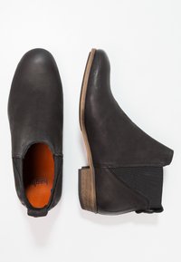 Ein Paar schwarze Leder-Chelsea-Stiefel mit braunen gestapelten Absätzen, elastischen seitlichen Einsätzen und orangefarbenen Einlegesohlen auf weißem Hintergrund.