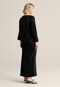 Sort satin kjole med langeærmer og en flydende, ankel-længde silhuet. Har en glat tekstur og minimalistisk design.