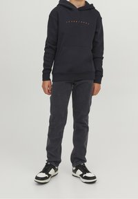 Marineblaue Kapuzenjacke mit einer Fronttasche und orangefarbigem Text, kombiniert mit dunkelgrauen Jeans und schwarz-weißen Sneakers. Einfaches, lässiges Design.