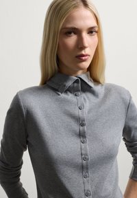 Grauer gerippter Strickoberteil mit kragenförmigem Ausschnitt, Knopfleiste und langen Ärmeln, mit eng anliegendem Schnitt und glatter Textur.