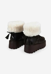 Botas de plataforma negras con puños de piel sintética blanca, forma redondeada, borlas decorativas y suelas gruesas y texturizadas.