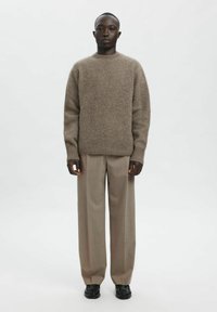 Beige strikkegenser med rund hals, ribbestrikkede mansjetter, kombinert med beige bukser og svarte sko. Plaggene har en ledig passform og myk tekstur.