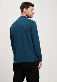 Koszulka polo z długim rękawem w kolorze teal z bawełny, z klasycznym kołnierzem, szwami po bokach u dołu oraz luźnym krojem.