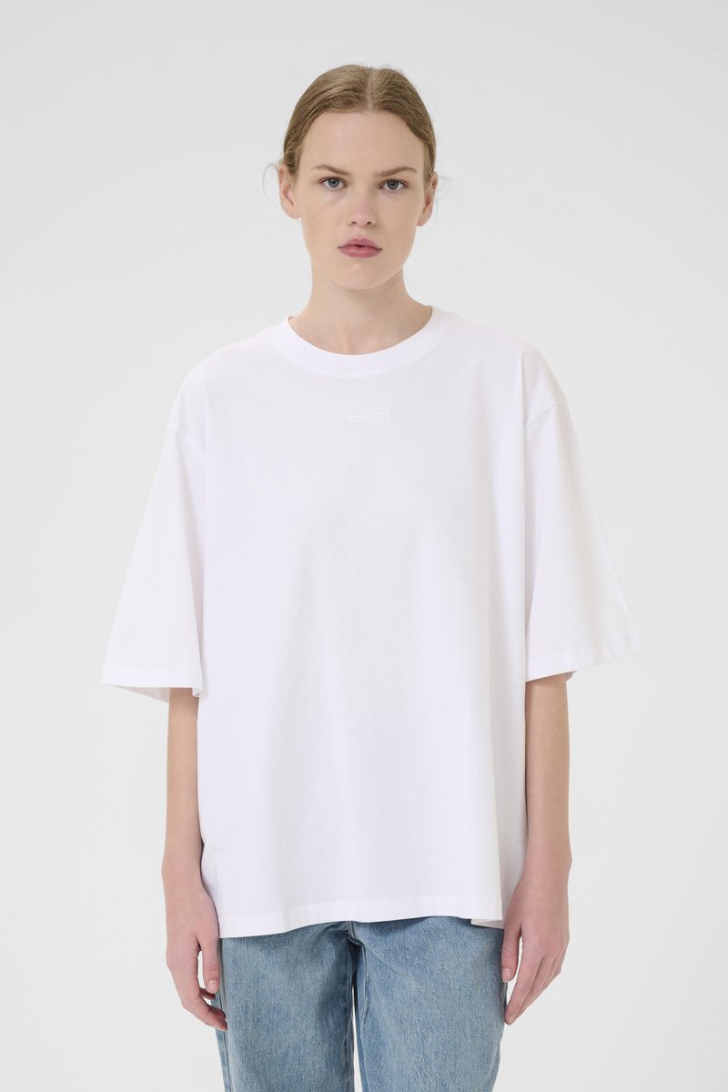 Witte katoenen t-shirt met een ronde hals en korte mouwen, voorzien van een klein logo in het midden. Gepaard met lichtblauwe denim jeans.