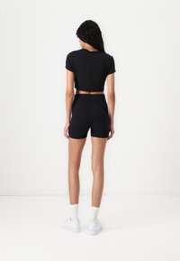 T-shirt noire courte associée à un short noir taille haute. Le matériau a l'air lisse ; le short est ajusté. Baskets blanches avec des chaussettes blanches.