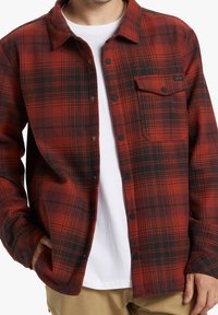 Red and black plaid flannel shirt with a button-up design, featuring a chest pocket, collared neck, and a soft texture.