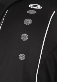 Top sportivo nero con accenti bianchi e una linea di motivi a puntini circolari lungo la parte anteriore per texture e dettaglio di design.