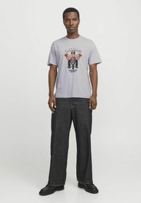 Lyse lilla t-shirt med korte ærmer og grafisk tryk af en karakter, parret med mørk denim brede bukser og sorte sko.