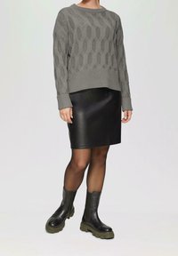Grå strikket sweater med struktureret mønster og ribbede manchetter, sammen med en sort læderskørt og sorte ankelstøvler med grøn sål.