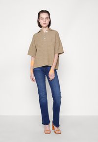 Beige pletená polo košile s krátkými rukávy, která má tři knoflíky a texturovaný vzor. Kombinováno s modrými džíny a oranžovými sandály na podpatku.